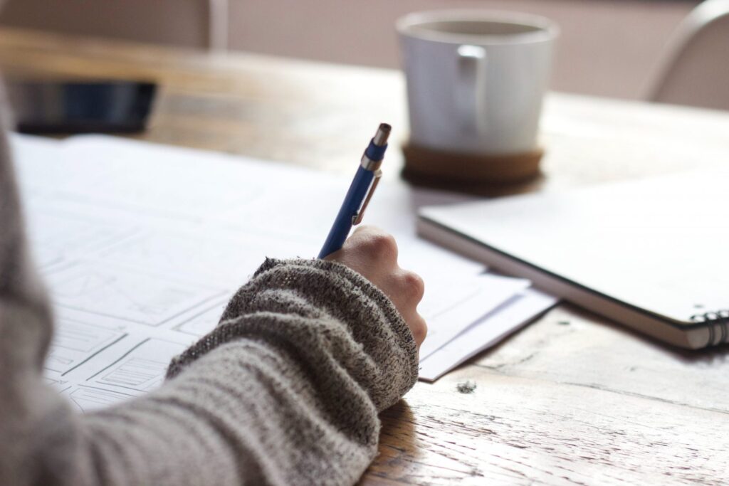 Woman writing notes with mug nearby. To represent how to get the most out of therapy.